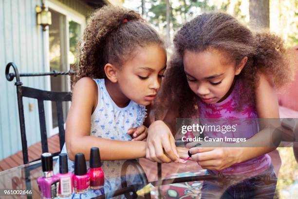 girl applying nail polish on sisters fingernails while sitting at table in yard - lackierte-fingernägel-finger stock-fotos und bilder