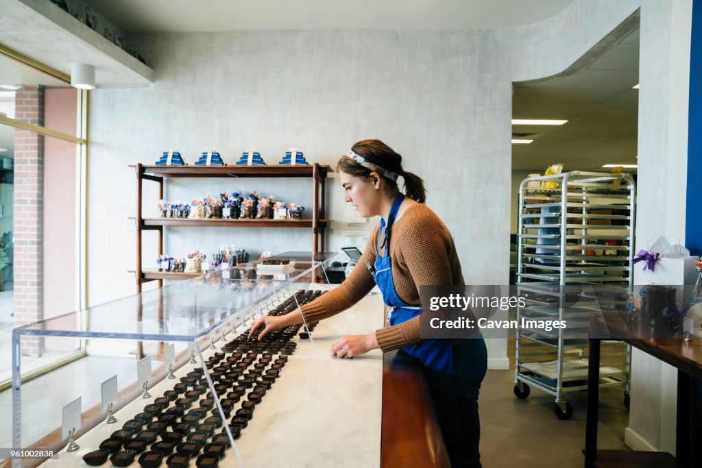 Side view of female owner arranging chocolates in display cabinet at store