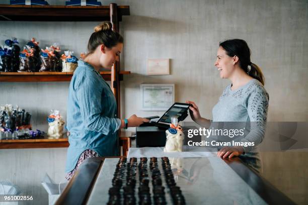 side view of owner laughing while female customer making mobile payment at store - choclate bar stock-fotos und bilder