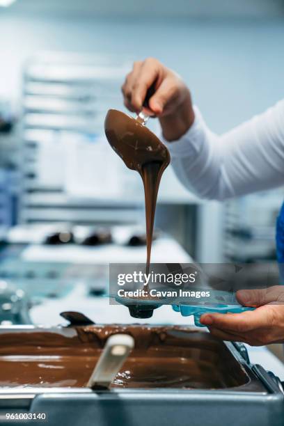 cropped hands of baker pouring chocolate in mold at factory - pasteleiro imagens e fotografias de stock