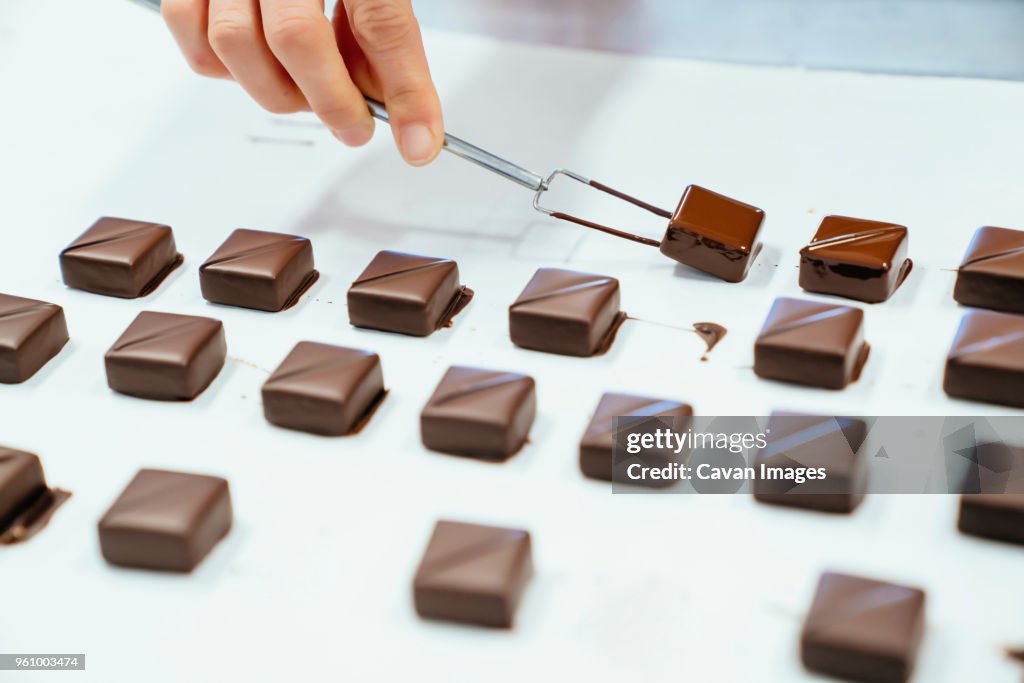 Cropped hand of chef holding chocolates with dipping fork in tray