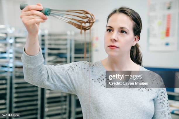 female chef looking at wire whisk while working in factory - wire whisk ストックフォトと画像