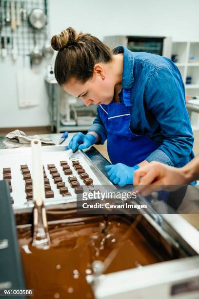 cropped hand of chef dipping chocolates in fondue while working with coworker in factory - pâtissier photos et images de collection