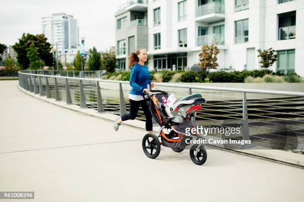 woman running with baby stroller on footpath in city - three wheeled pushchair stock pictures, royalty-free photos & images
