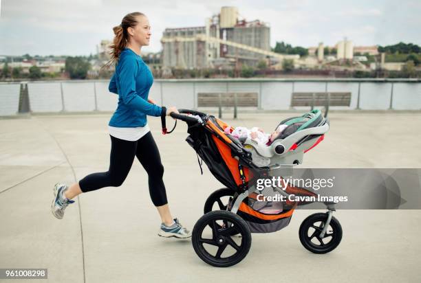 side view of woman pushing baby stroller while jogging in city - baby stroller fotografías e imágenes de stock