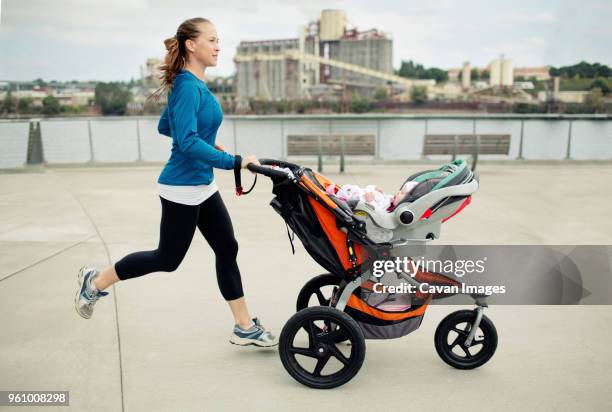 side view of woman pushing baby stroller while jogging in city - mother running stockfoto's en -beelden