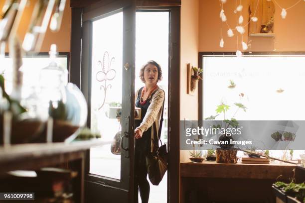 female customer carrying plants in crate while standing at doorway of garden center - entrando fotografías e imágenes de stock
