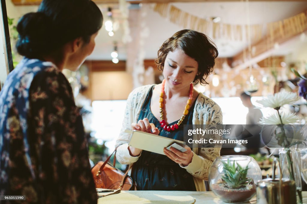 Owner looking at customer making card payment at counter in plant shop