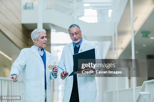 Male doctors discussing over laptop computer in hospital corridor Male doctors discussing over laptop computer in hospital corridor