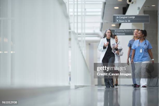 female doctors discussing while walking in hospital corridor - gang stockfoto's en -beelden