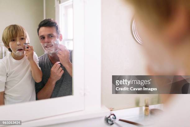father and son shaving while reflecting in mirror - man shaving face stock-fotos und bilder