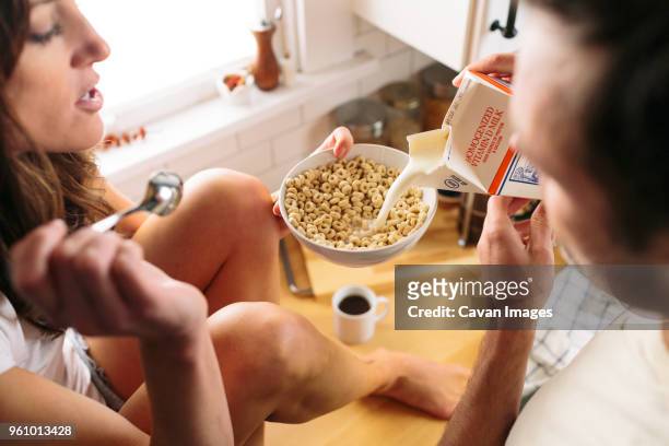 man pouring milk in bowl with breakfast cereal held by woman - cheerios stock-fotos und bilder