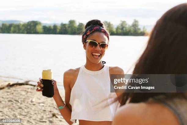 happy woman holding can while looking at friend against river - beer flowing stock pictures, royalty-free photos & images