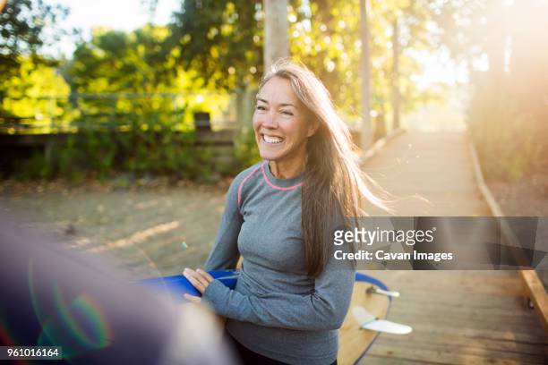 smiling woman with paddleboard looking away while walking on boardwalk - paddelbrett stock-fotos und bilder
