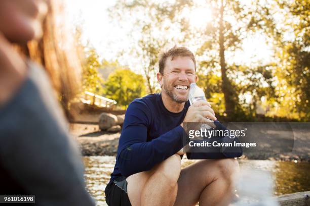 portrait of man drinking water while sitting with woman on pier - sport drinking bottle stock-fotos und bilder