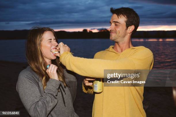 man feeding smore to female friends against river during sunset - sky crackers stock pictures, royalty-free photos & images