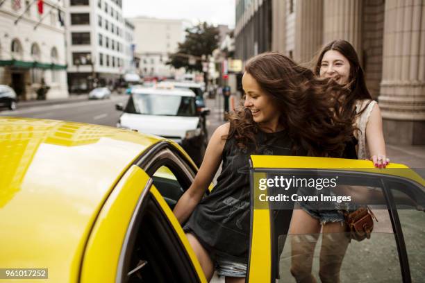 smiling female friends entering in taxi - entrar fotografías e imágenes de stock