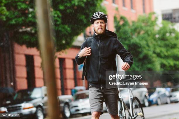 male commuter looking away while walking in city during rainy season - center of gravity 2017 stock pictures, royalty-free photos & images