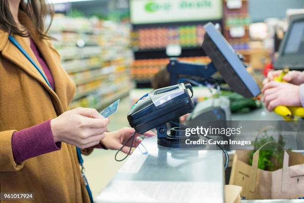 midsection of woman paying bill with credit card while standing by counter at supermarket - kasse supermarkt stock-fotos und bilder