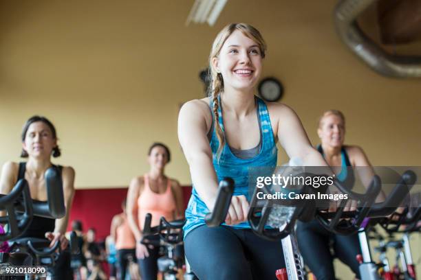 smiling women cycling on exercise bikes at gym - cours de spinning photos et images de collection