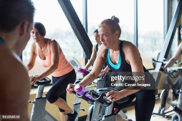 male instructor guiding women cycling on exercise bikes at gym - stationary cycling class stock pictures, royalty-free photos & images