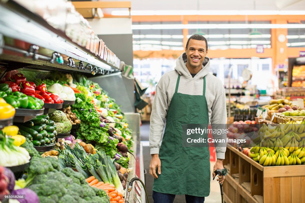 Portrait of smiling worker standing by shelves at supermarket