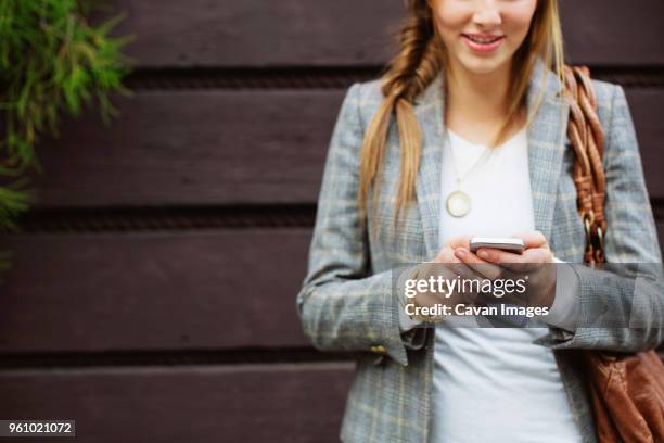 midsection of woman using mobile phone against wall in city - fishtail braid stock pictures, royalty-free photos & images