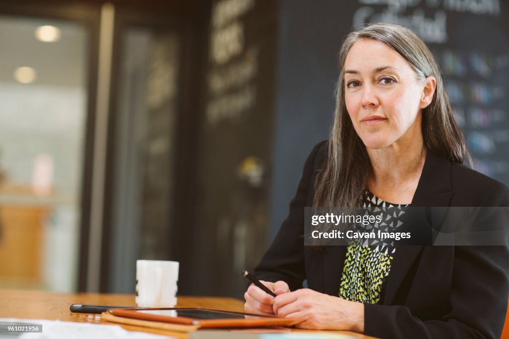 Portrait of confident businesswoman sitting at table with tablet computer in office