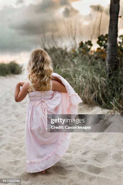 rear view of girl holding dress while standing on sand at beach - peoria illinois stock pictures, royalty-free photos & images