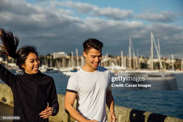 happy young couple jogging while exercising on promenade against cloudy sky in city - boardwalk australia stock pictures, royalty-free photos & images