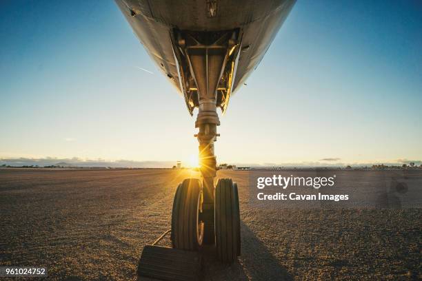 cropped airplane at runway against sky during sunset - landing gear stock-fotos und bilder