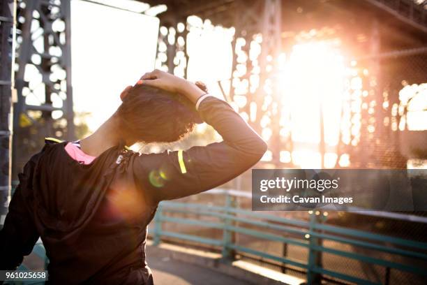 rear view of female jogger stretching neck on footbridge during sunny day - neck stretch stock pictures, royalty-free photos & images