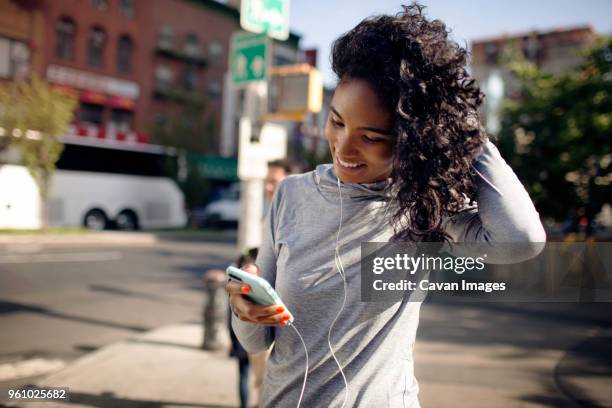 happy woman using smart phone while standing on street - happy people running stockfoto's en -beelden