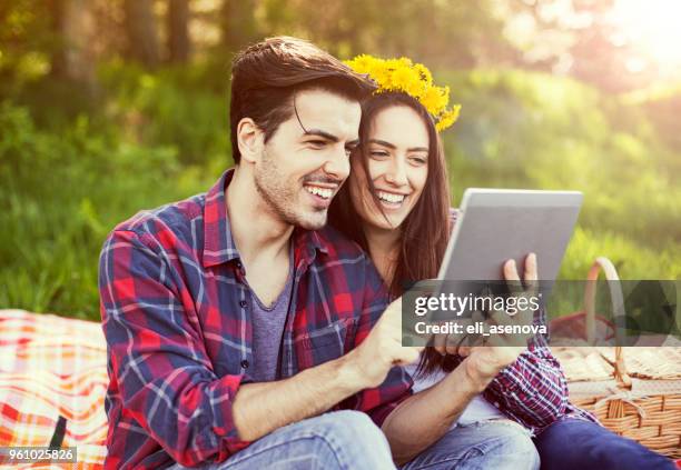 beautiful young couple using tablet during picnic outdoor - deitar se imagens e fotografias de stock