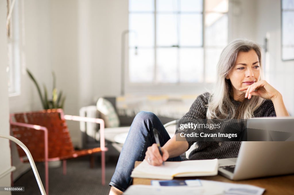 Mature woman writing in diary while working at home