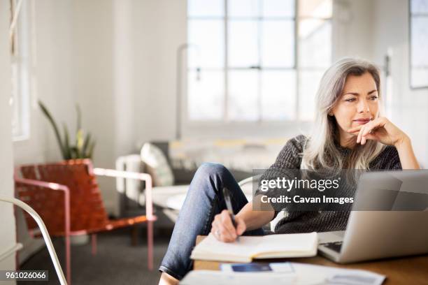 mature woman writing in diary while working at home - mature adult computer stock pictures, royalty-free photos & images