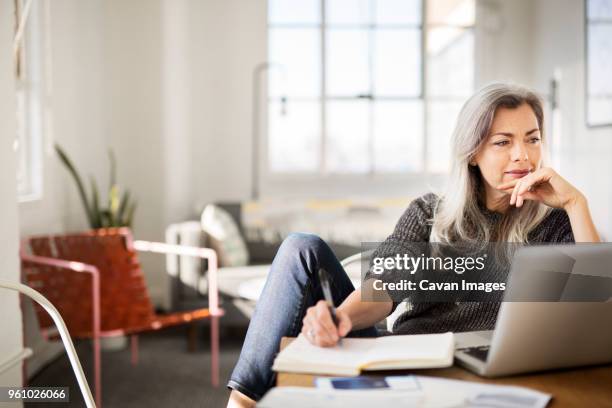 mature woman writing in diary while working at home - medelålders kvinnor bildbanksfoton och bilder