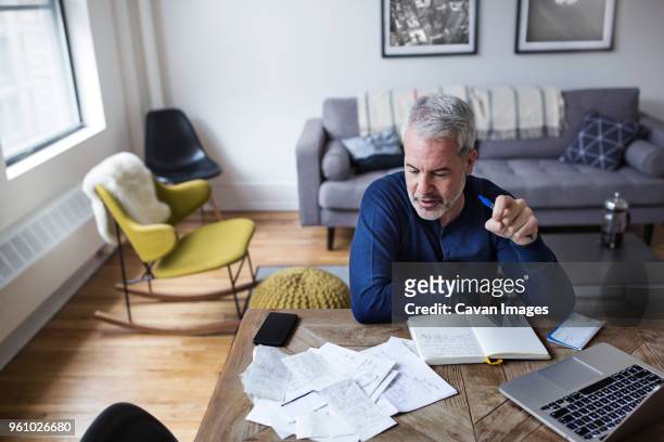 high angle view of mature man analyzing bills at table in home - financial planner stockfoto's en -beelden