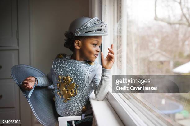 curious boy dressed up in armor costume looking out through window at home - traditional armour stock pictures, royalty-free photos & images
