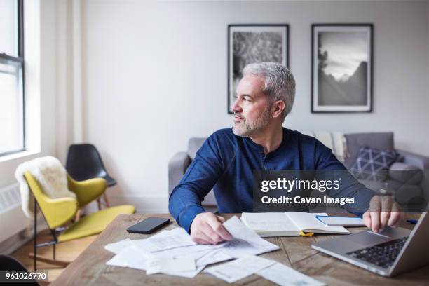 thoughtful man looking away while calculating home finances at table - home inspection photos et images de collection