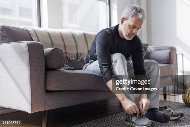 full length of mature man wearing sports shoe at home - sports footwear stock-fotos und bilder