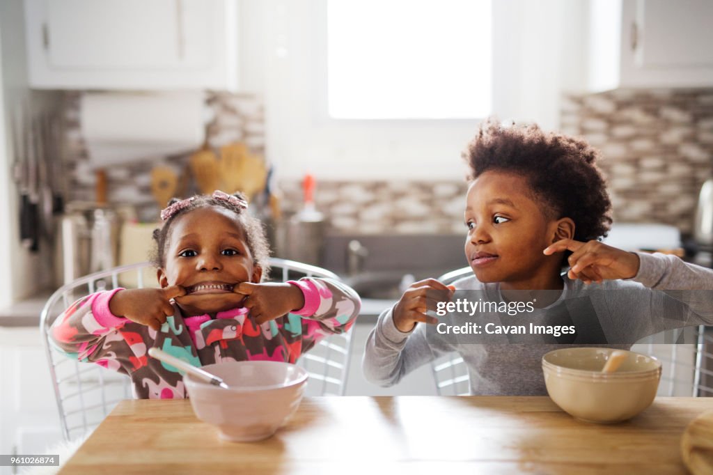 Portrait of playful girl making face while brother looking at her in kitchen