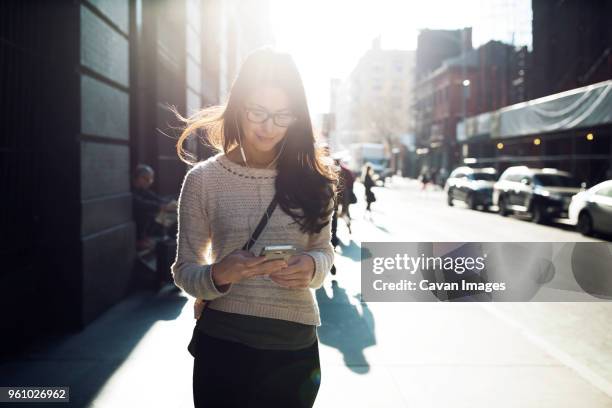 young woman listening music through smart phone on city street - music from the motor city stock pictures, royalty-free photos & images