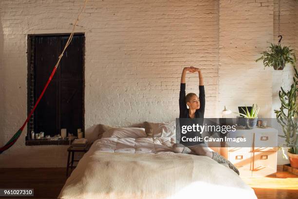 young woman stretching arms while sitting on bed at home - morning bed stretch stock pictures, royalty-free photos & images