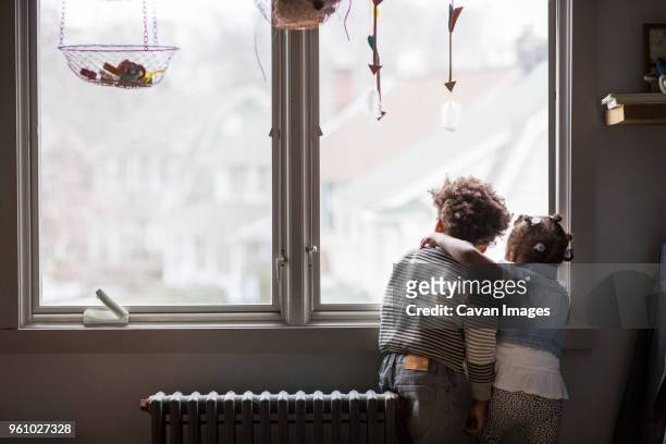 rear view of siblings looking through window at home - family rear view stock pictures, royalty-free photos & images