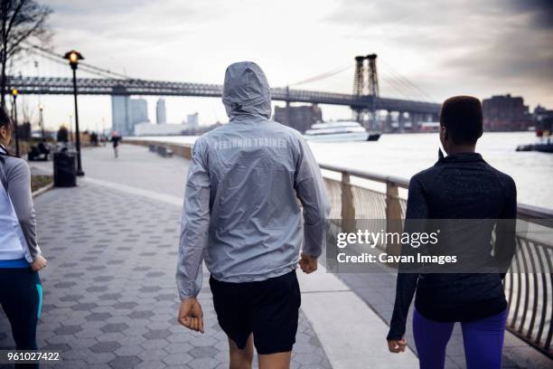 rear view of athletes walking on footpath with williamsburg bridge in background - williamsburg new york city stock pictures, royalty-free photos & images