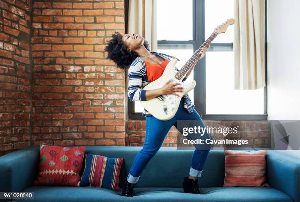 happy woman singing while playing guitar on sofa - woman musician stock pictures, royalty-free photos & images