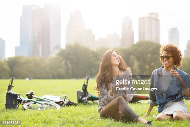 happy friends talking while sitting on grassy field - adult riding bike through park stockfoto's en -beelden
