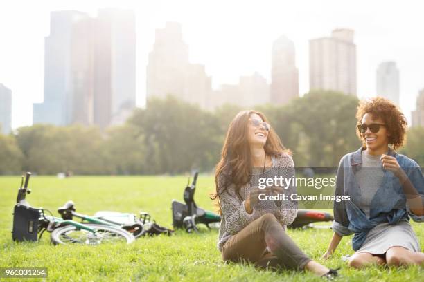 happy friends talking while sitting on grassy field - adult riding bike through park stock pictures, royalty-free photos & images