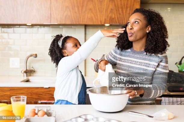 playful mother and daughter mixing batter with electric whisk in kitchen - fond orange fotografías e imágenes de stock